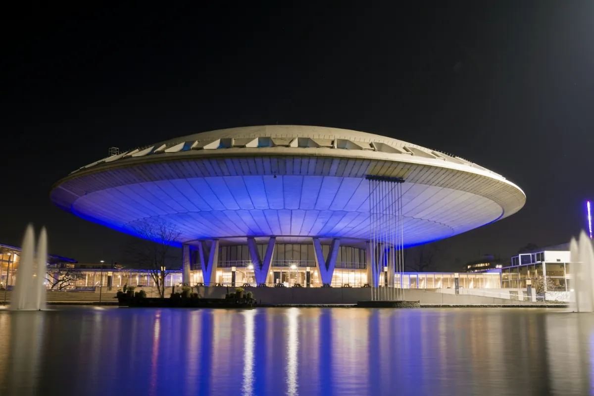 Het Evoluon in Eindhoven, blauw verlicht in de avond en weerspiegeld in de vijver